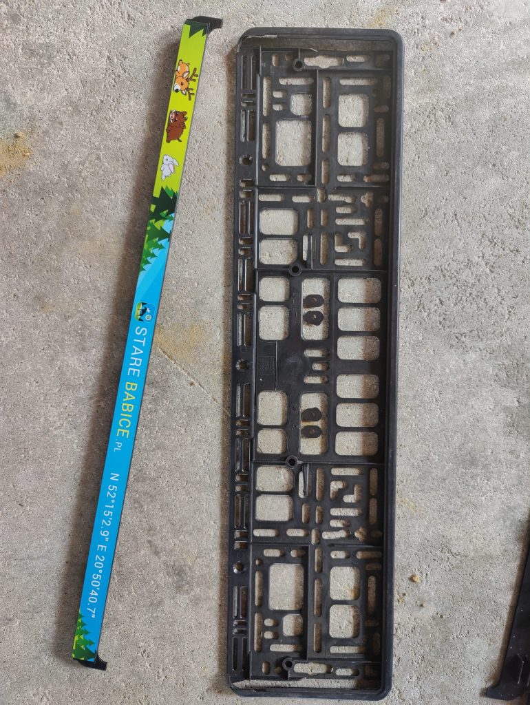 Ramka rejestracyjna Stare Babice położona na betonie obok czarnej podstawy tablicy.